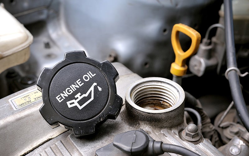 Close-up of a black engine oil cap resting next to an open oil filler