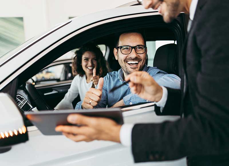 A happy couple gives thumbs up while sitting in a new car